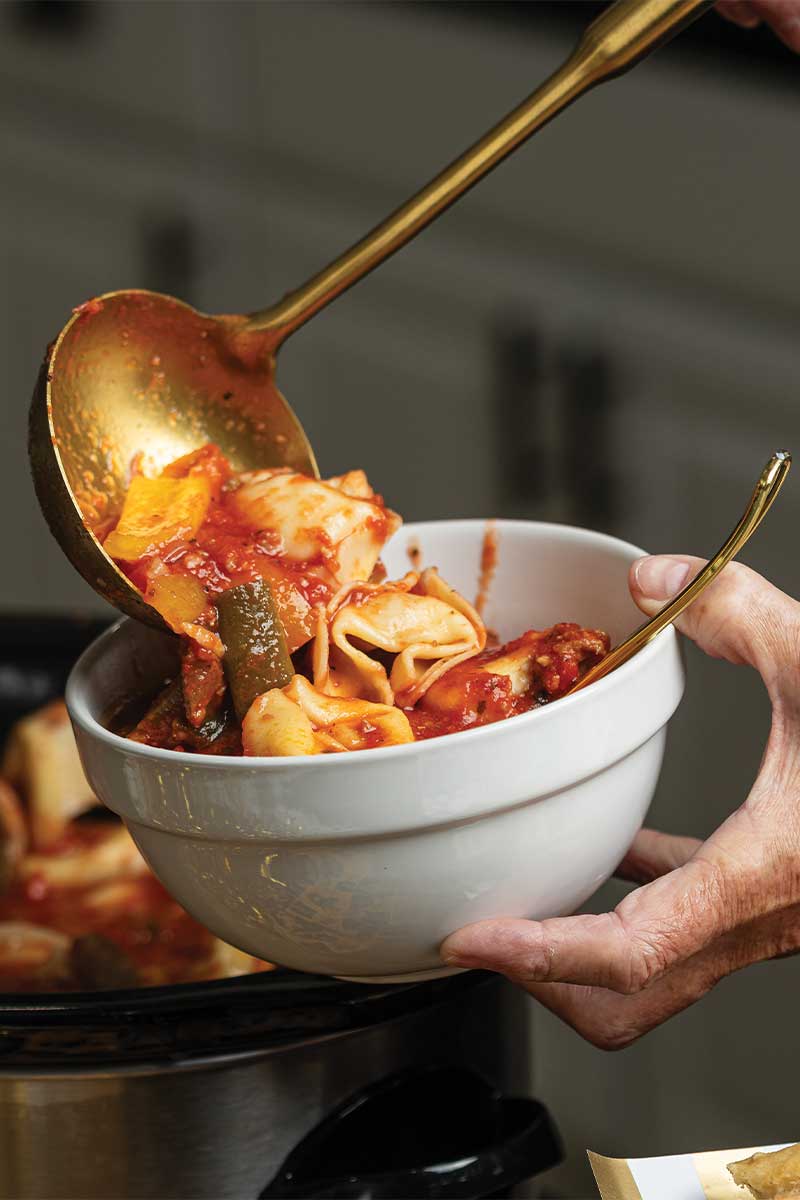Scooping Easy tortellini sausage stew into bowl