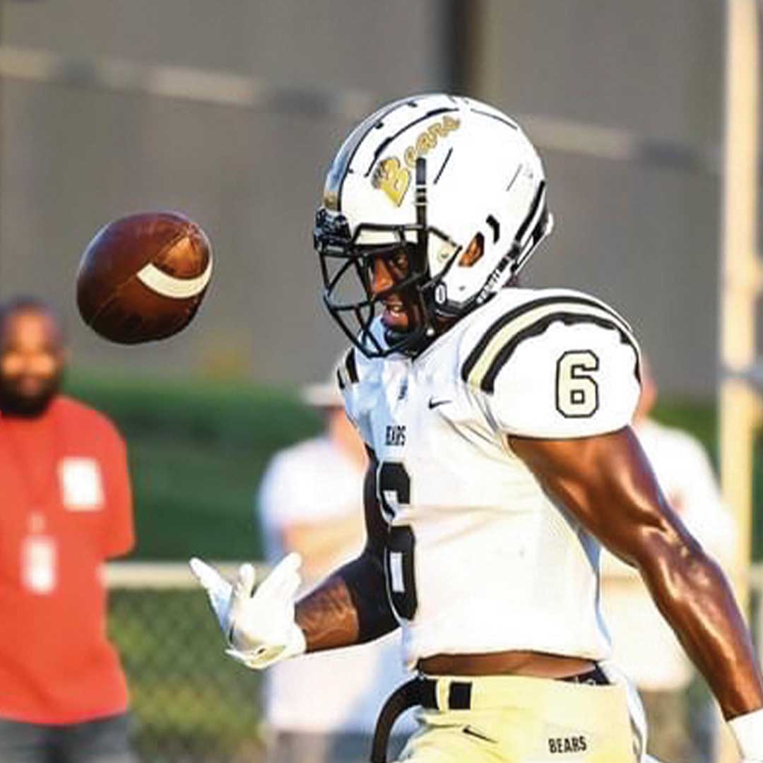 Football player tossing up a football while walking